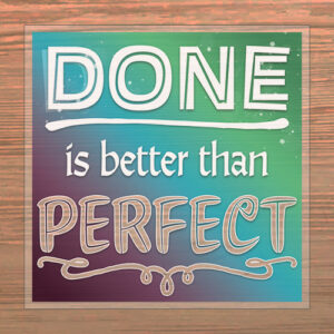 A sign with a gradient blue and green background displays the phrase “DONE is better than PERFECT” in bold, stylized white and beige letters. The sign is set against a wooden surface.
