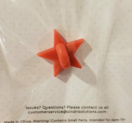 A Pen-Dragon Enamel Pin, Sticker, or Magnet displayed on clear packaging; features a red five-pointed star shape with a central circular loop. Text below gives contact info and a small parts warning.